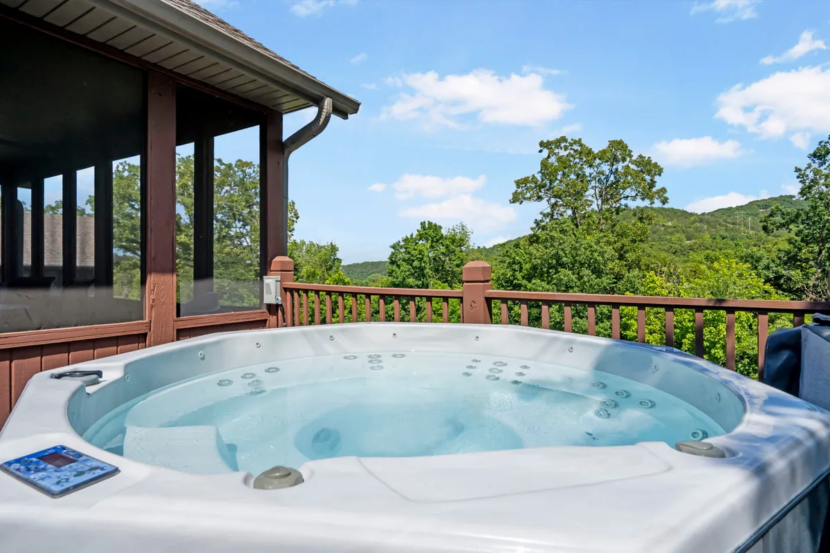 An exterior view of a private hot tub situated on a deck with wooden railings, overlooking a scenic valley. The inviting hot tub is positioned to maximize the enjoyment of nature views, whether relaxing solo or with friends.