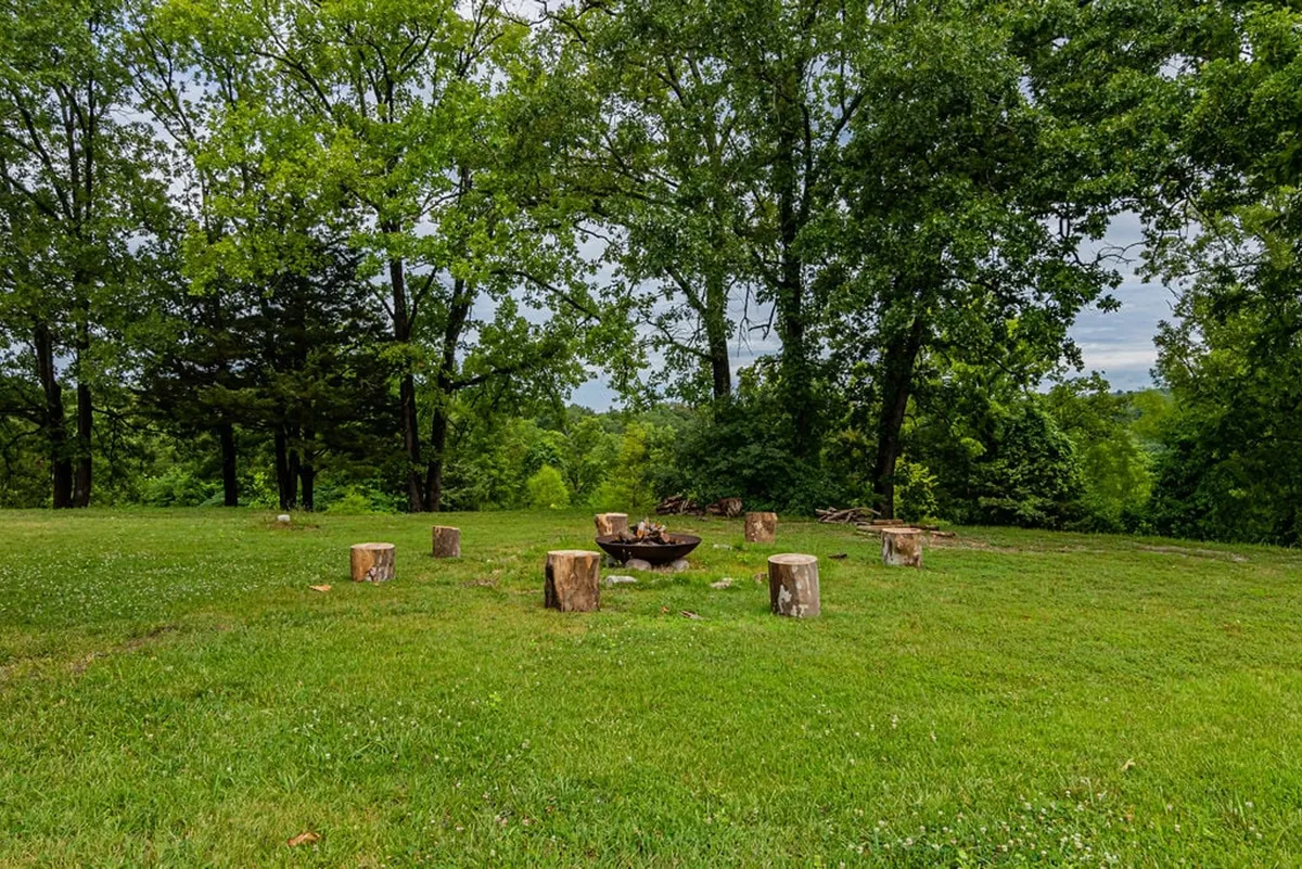 A cozy fire pit surrounded by logs for seating, nestled among the trees. The inviting scene suggests evenings spent telling stories, roasting marshmallows, and stargazing as a group.