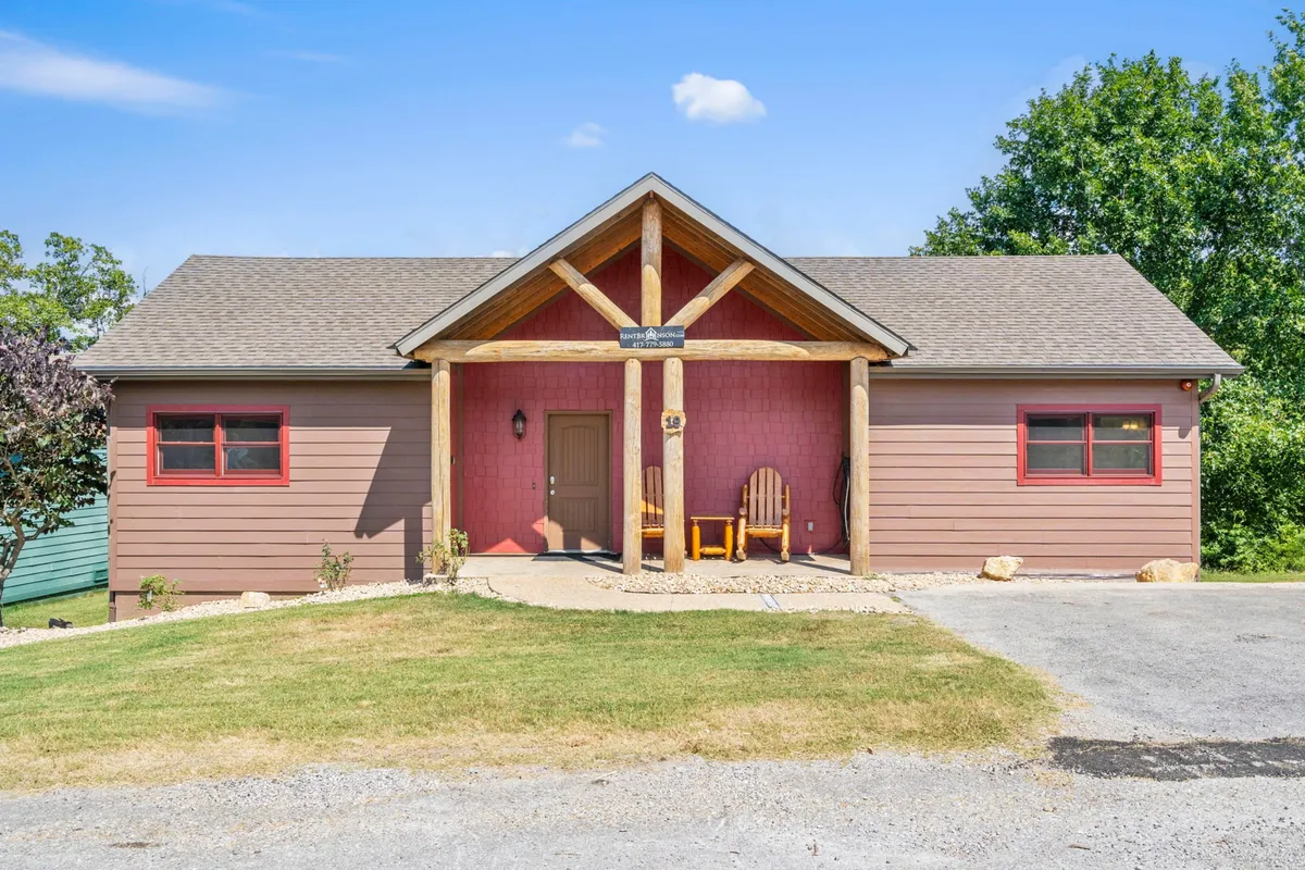 This exterior image showcases the front porch of the property, complete with inviting wooden chairs and decorative beams. The entrance door and cozy porch setting are surrounded by natural greenery, hinting at the peaceful environment guests can enjoy despite nearby construction.