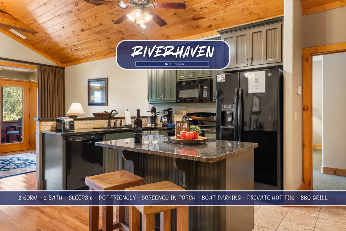 A modern kitchen featuring a granite countertop island, stainless steel appliances, a view into the adjacent dining area, and warm wooden accents. The scene captures preparations for group meals and the easy flow between cooking and socializing spaces.