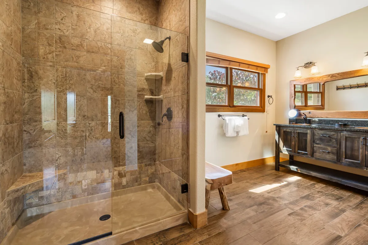 A serene bathroom scene featuring a glass shower enclosure, wooden vanity, and natural light entering through the window. The atmosphere is tranquil and rejuvenating, emphasizing comfort and relaxation after a day of adventure.