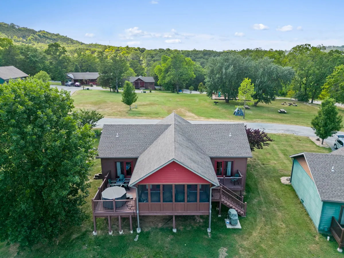 A large outdoor deck area with red accents on the house, set among tall trees. The expansive space is ideal for family gatherings, outdoor dining, and barbecues, with ample room for children to play in the open area.